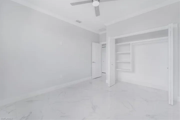 Unfurnished bedroom with light marble finish flooring, crown molding, a closet, and ceiling fan