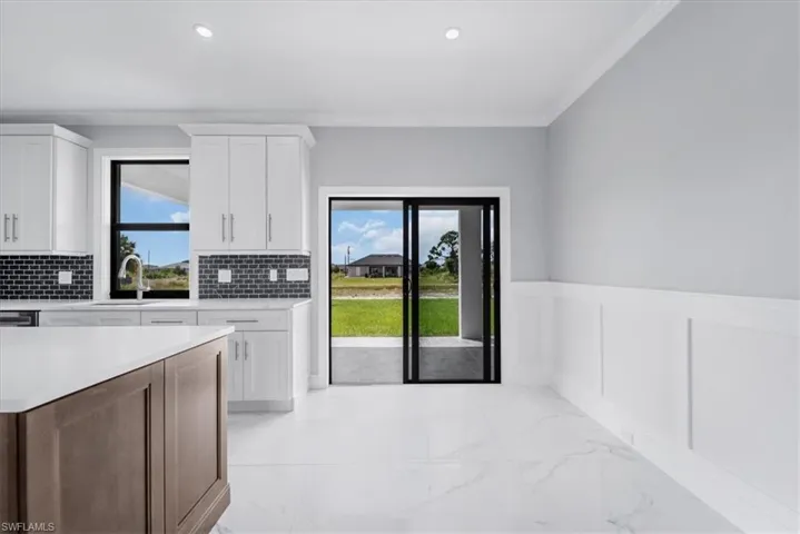 Kitchen featuring a wainscoted wall, a decorative wall, dual tone cabinetry, crown molding, and light marble finish floors