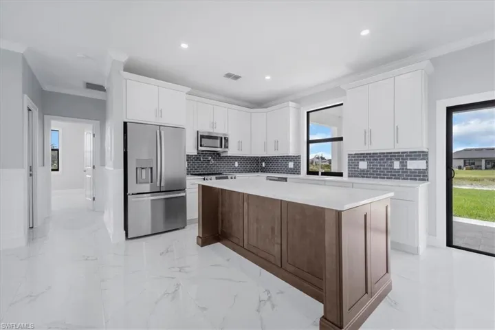 Kitchen featuring crown molding, stainless steel appliances, a kitchen island, recessed lighting, and light stone countertops