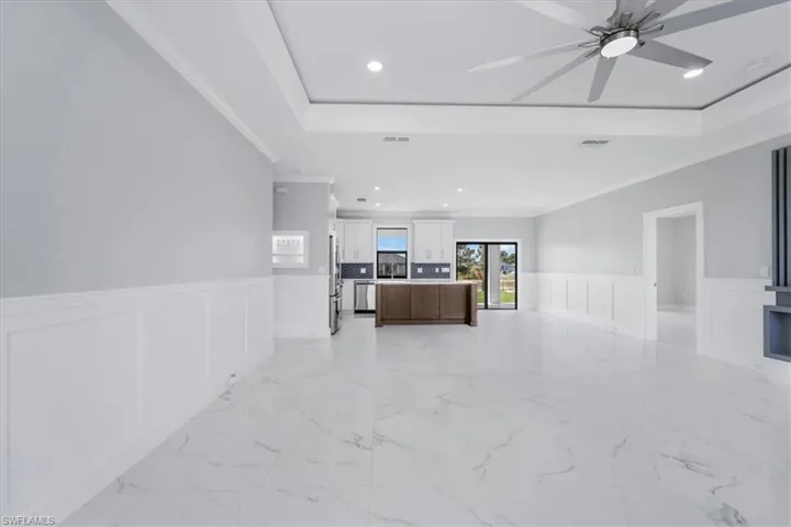 Unfurnished living room featuring wainscoting, a decorative wall, a ceiling fan, crown molding, and recessed lighting