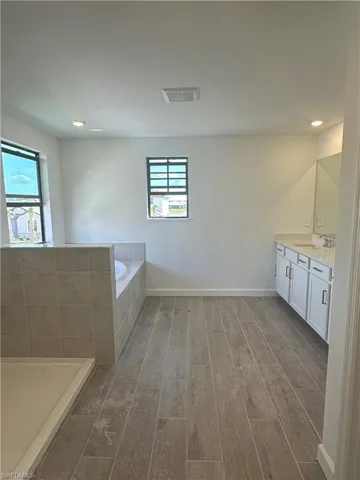 Bathroom with a relaxing tiled bath, plenty of natural light, hardwood / wood-style floors, and vanity
