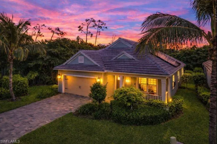View of front of house with a porch, a tile roof, driveway, a front lawn, and a garage