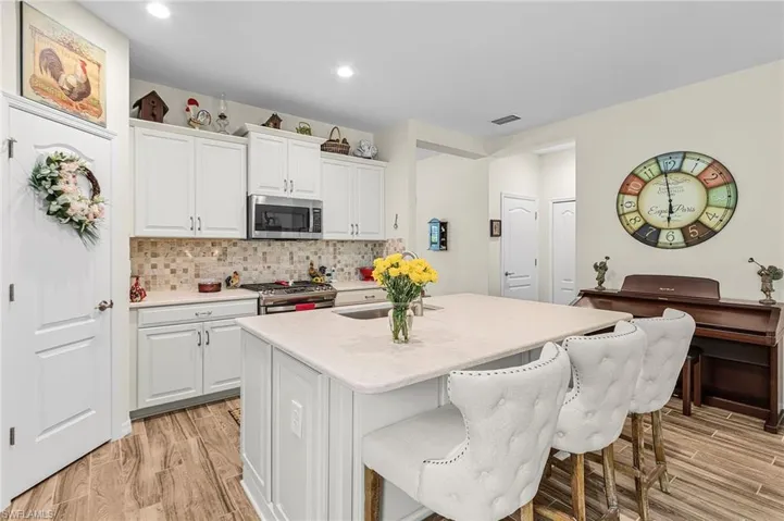 Kitchen featuring white cabinets, tasteful backsplash, stainless steel appliances, a center island with sink, and a breakfast bar area