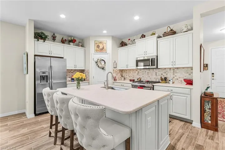 Kitchen with white cabinetry, stainless steel appliances, a kitchen breakfast bar, backsplash, and recessed lighting