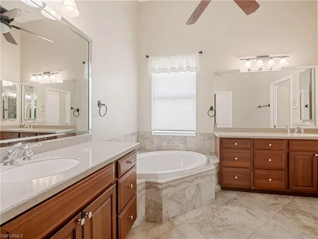 Bathroom with a relaxing tiled tub, ceiling fan, tile patterned floors, and dual vanity