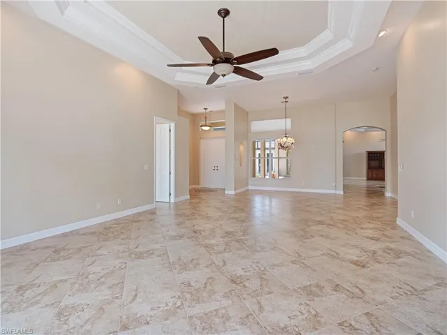Unfurnished living room with ceiling fan with notable chandelier, tile patterned flooring, and a tray ceiling