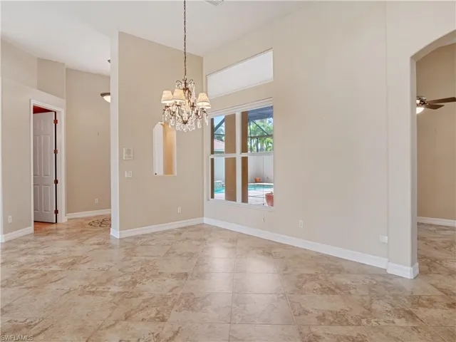 Tiled spare room featuring ceiling fan with notable chandelier