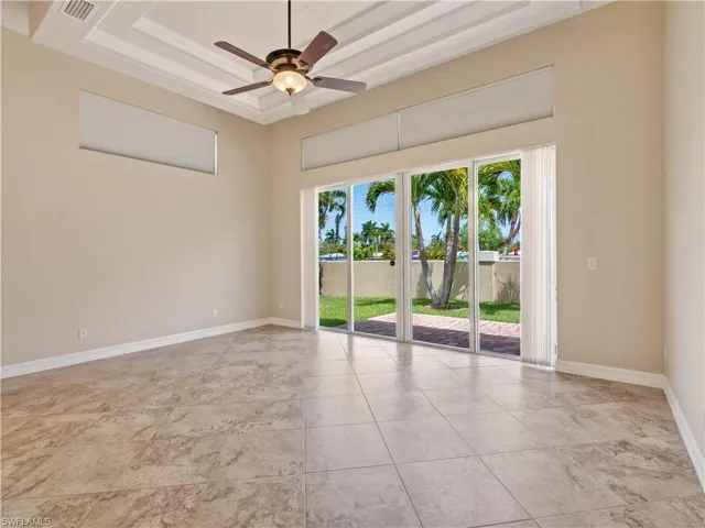 Empty room with light tile patterned flooring, ceiling fan, and a raised ceiling