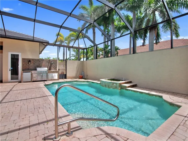 View of swimming pool featuring a patio, glass enclosure, grilling area, and an outdoor kitchen