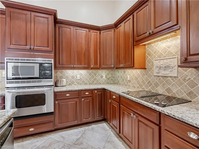 Kitchen with decorative backsplash, appliances with stainless steel finishes, light stone counters, and light tile patterned floors
