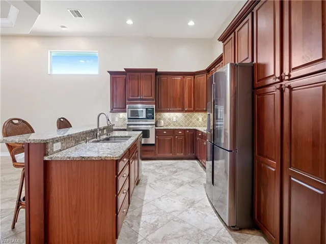 Kitchen with a kitchen bar, tasteful backsplash, stainless steel appliances, sink, and light tile patterned floors