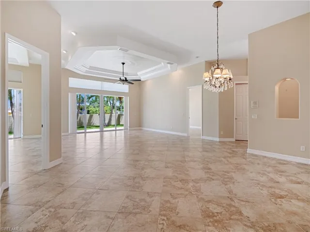 Spare room featuring ceiling fan with notable chandelier, light tile patterned floors, and a tray ceiling