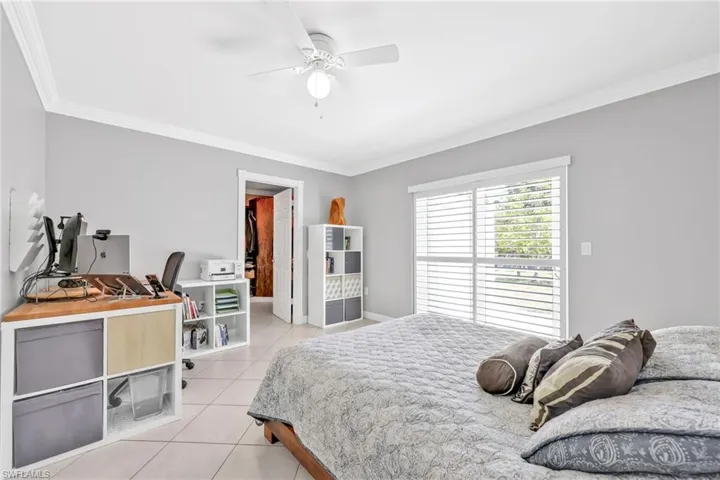 Bedroom with light tile patterned floors, crown molding, an office area, a ceiling fan, and baseboards
