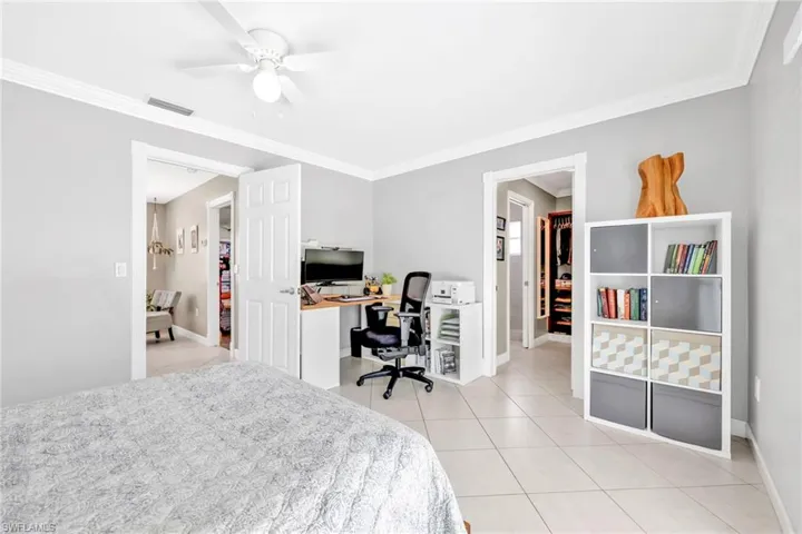 Bedroom featuring an office area, baseboards, crown molding, light tile patterned flooring, and a ceiling fan