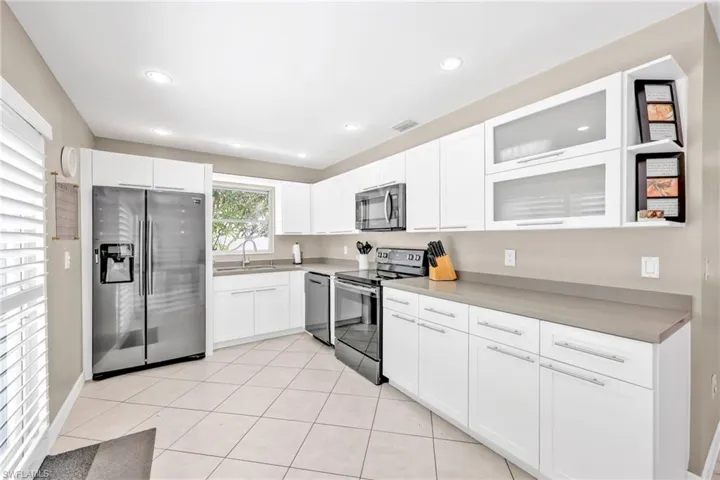 Kitchen with appliances with stainless steel finishes, a sink, white cabinetry, glass insert cabinets, and recessed lighting