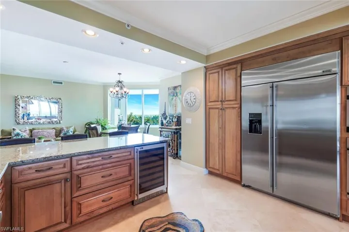 Kitchen featuring light tile flooring, a notable chandelier, built in fridge, wine cooler, and light stone countertops