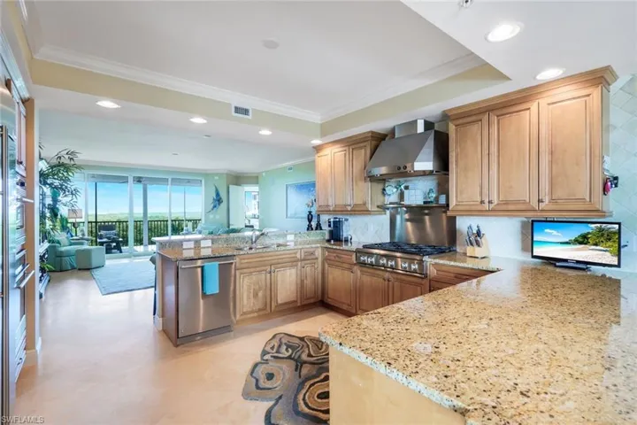 Kitchen with kitchen peninsula, stainless steel appliances, tasteful backsplash, light stone countertops, and wall chimney exhaust hood