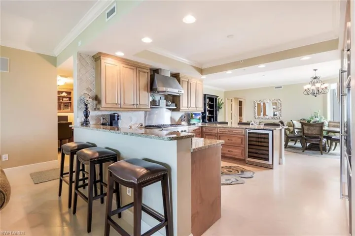 Kitchen featuring kitchen peninsula, wall chimney exhaust hood, beverage cooler, backsplash, and a breakfast bar