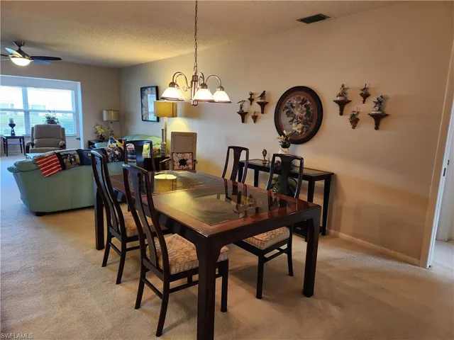 Dining space featuring a textured ceiling, ceiling fan with notable chandelier, and light colored carpet