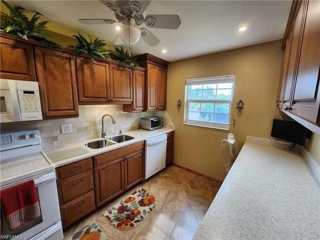 Kitchen featuring white appliances, backsplash, sink, ceiling fan, and light tile floors