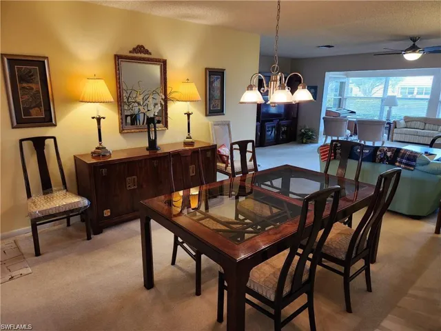 Carpeted dining area featuring a textured ceiling and ceiling fan with notable chandelier