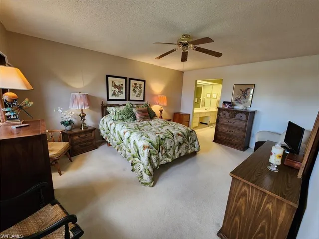 Carpeted bedroom with ensuite bathroom, ceiling fan, and a textured ceiling