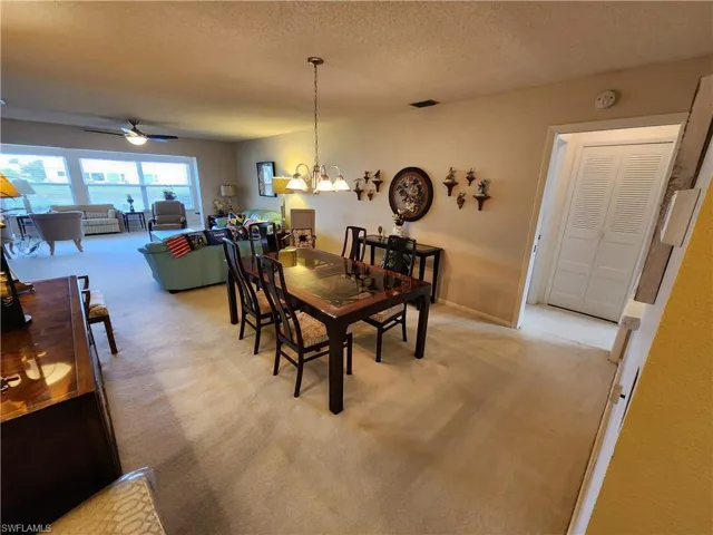 Dining space featuring a textured ceiling, carpet flooring, and ceiling fan with notable chandelier