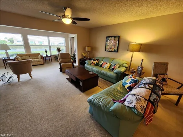 Living room featuring ceiling fan, a textured ceiling, and carpet flooring