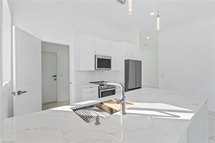 Kitchen featuring light stone counters, white cabinetry, stainless steel appliances, hanging light fixtures, and recessed lighting