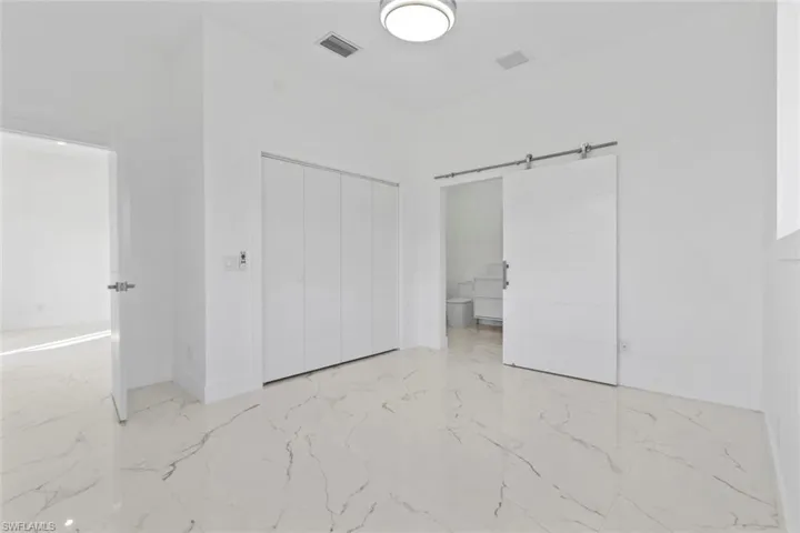 Master bedroom with a barn door, light marble finish flooring, connected bathroom, and a closet