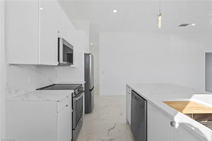 Kitchen featuring white cabinets, appliances with stainless steel finishes, light stone countertops, light marble finish flooring, and recessed lighting