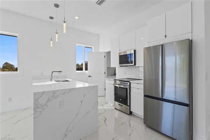 Kitchen featuring appliances with stainless steel finishes, hanging light fixtures, white cabinets, light marble finish flooring, and recessed lighting