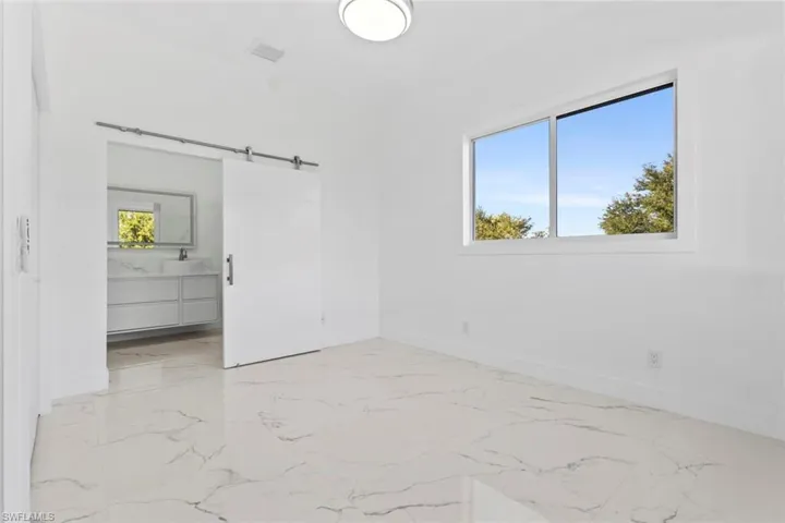 Master bedroom featuring a barn door, multiple windows, light marble finish floors, and ensuite bath