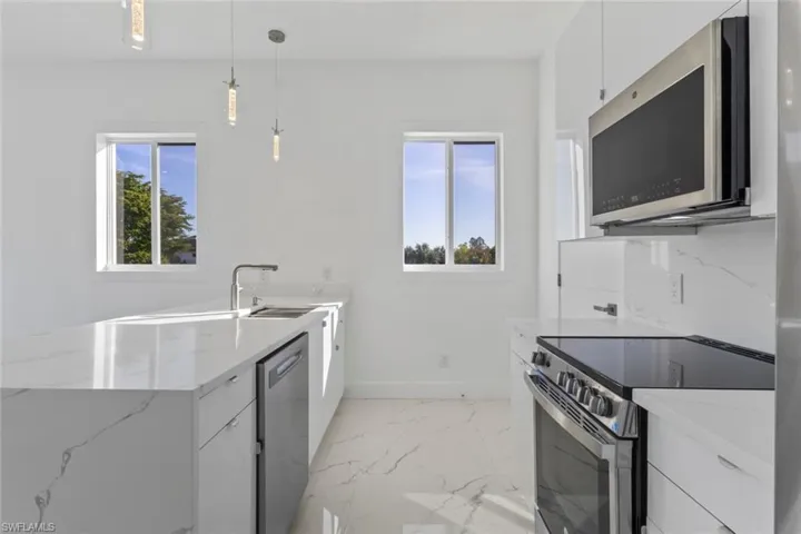Kitchen with white cabinets, stainless steel appliances, a peninsula, decorative light fixtures, and light stone countertops