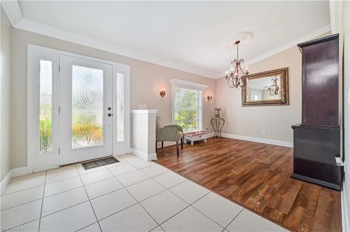 Foyer with light hardwood / wood-style floors, a notable chandelier, ornamental molding, and lofted ceiling