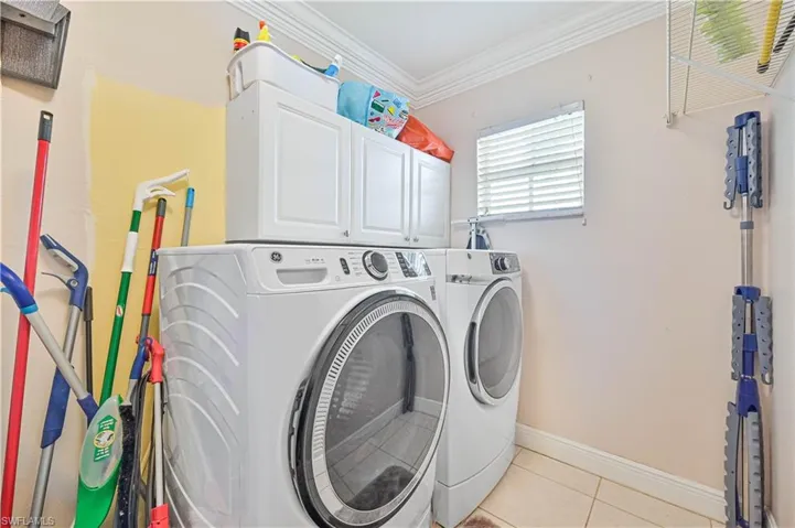 Laundry area with independent washer and dryer, crown molding, light tile patterned floors, and cabinets