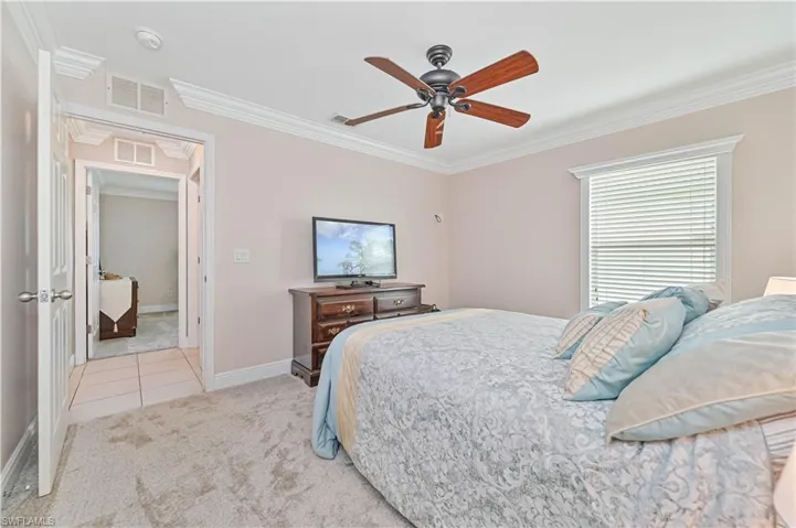 Bedroom with ceiling fan, ornamental molding, and light colored carpet