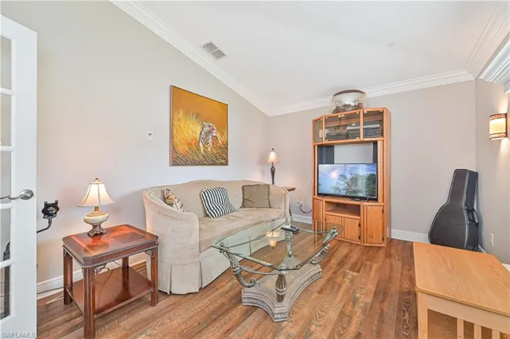 Living room with dark hardwood / wood-style floors, vaulted ceiling, and ornamental molding