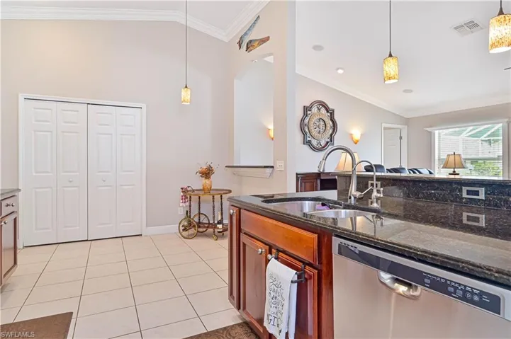 Kitchen featuring dark stone counters, pendant lighting, dishwasher, light tile patterned floors, and sink