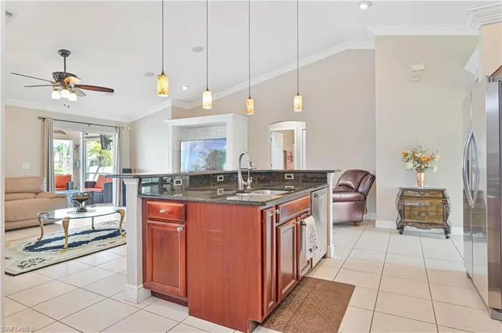 Kitchen with dark stone counters, ornamental molding, a kitchen island with sink, ceiling fan, and stainless steel appliances