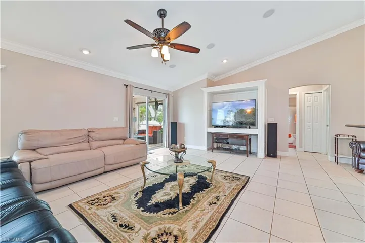 Tiled living room with ceiling fan, vaulted ceiling, and ornamental molding
