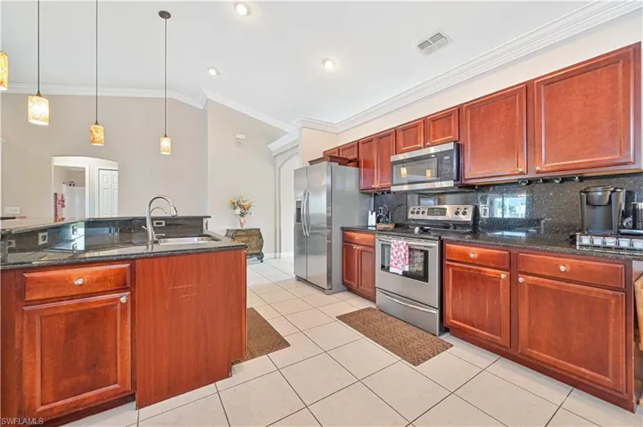Kitchen featuring dark stone counters, decorative light fixtures, decorative backsplash, light tile patterned floors, and stainless steel appliances