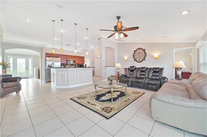 Living room featuring ceiling fan, vaulted ceiling, ornamental molding, and light tile patterned floors