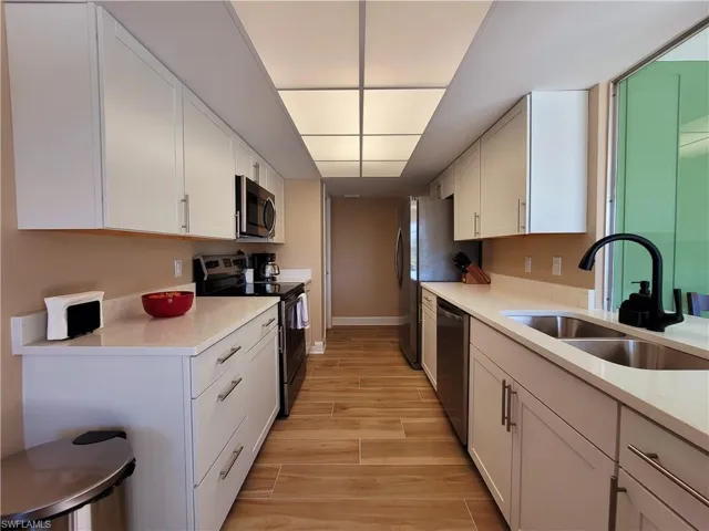 Galley kitchen featuring white cabinetry, light-toned countertops, wood-finish flooring, stainless steel appliances, and a double basin sink with a matte black faucet