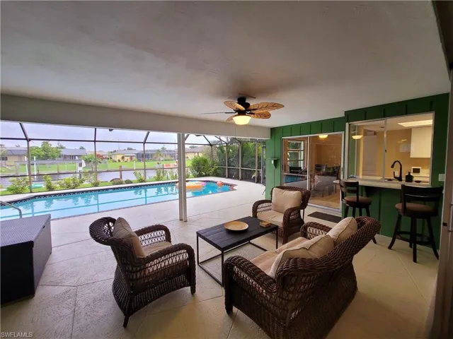 Screened-in lanai featuring a swimming pool, textured concrete patio, ceiling fan, and a pass-through bar