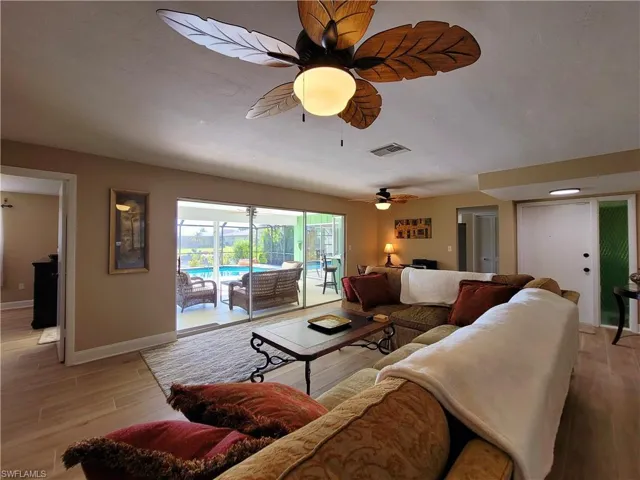 Open concept living area featuring wood-finish flooring, a tropical-style ceiling fan, and sliding glass doors leading to an outdoor screened patio with a pool