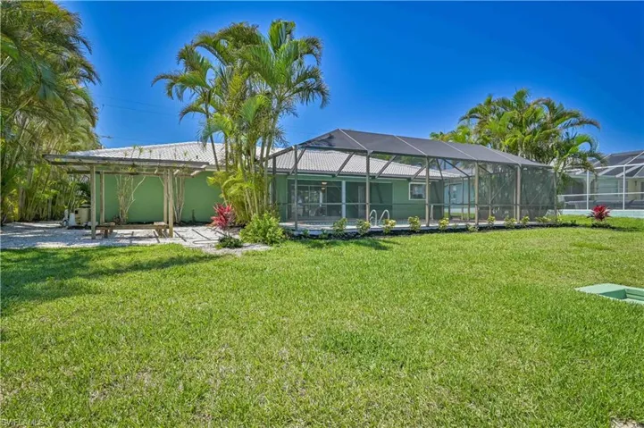 Expansive green lawn featuring a screened pool enclosure, a wooden pergola, and established palm trees