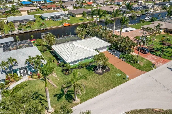 Waterfront property featuring a canal, private boat dock, mature landscaping, and a paved driveway