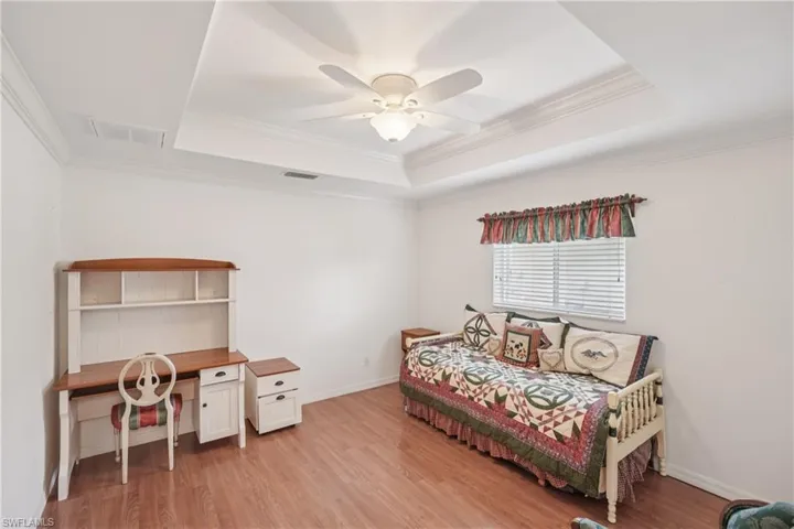 Guest bedroom 1 featuring a raised ceiling, ornamental molding, light wood-style flooring, and ceiling fan