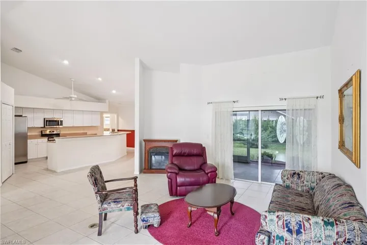 Living room featuring high vaulted ceiling, light tile patterned floors, a glass covered fireplace, plenty of natural light, and ceiling fan